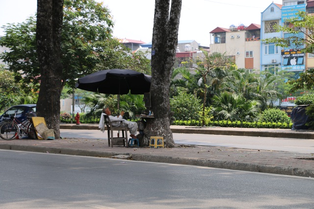 Dưới bóng cây xà cừ cổ thụ ở vỉa hè đường Láng, những quán cắt tóc vỉa hè còn mở thêm ô dù để tránh bớt cái nắng nóng của mùa hè đang đến.